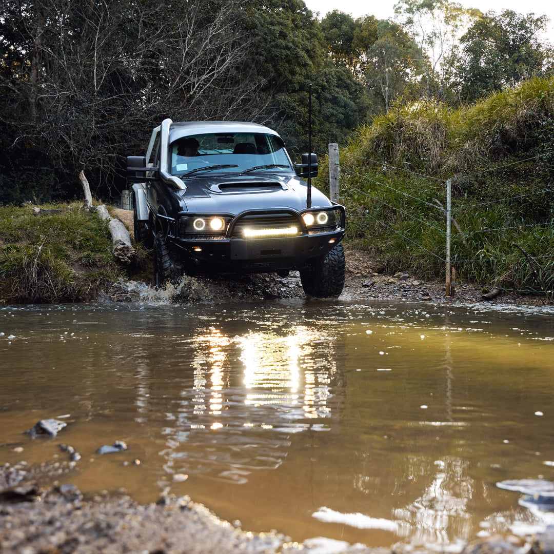 Black off-road vehicle crossing a muddy water crossing in a farm creek.